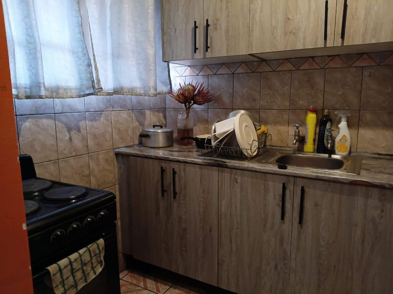 A functional kitchen featuring wood-look laminate cabinetry, a stainless steel sink, tiled backsplash, and a freestanding electric stove.