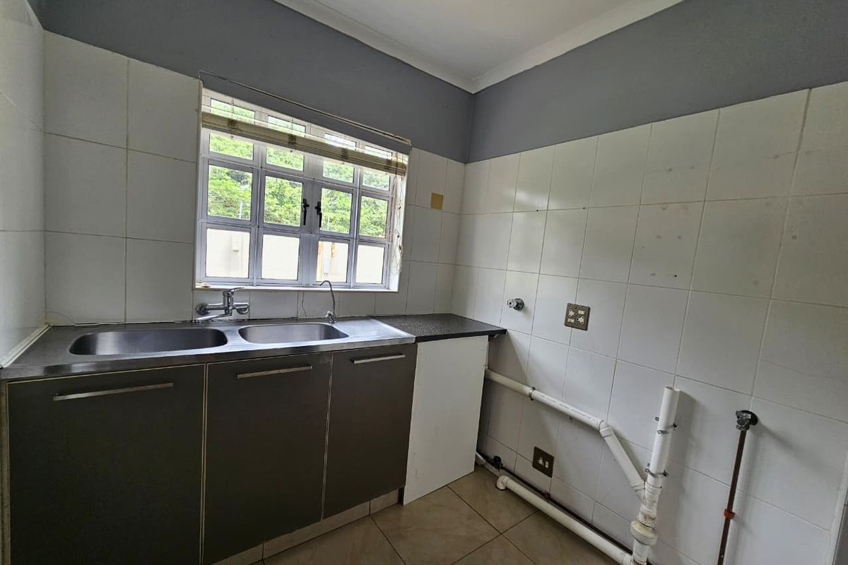 A functional kitchen area featuring a double stainless steel sink, tiled splashbacks, and exposed plumbing connections ready for appliance installation.