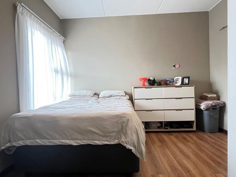 A functional bedroom featuring laminate flooring and a window with a curtain rail, offering a neutral base for personalization.