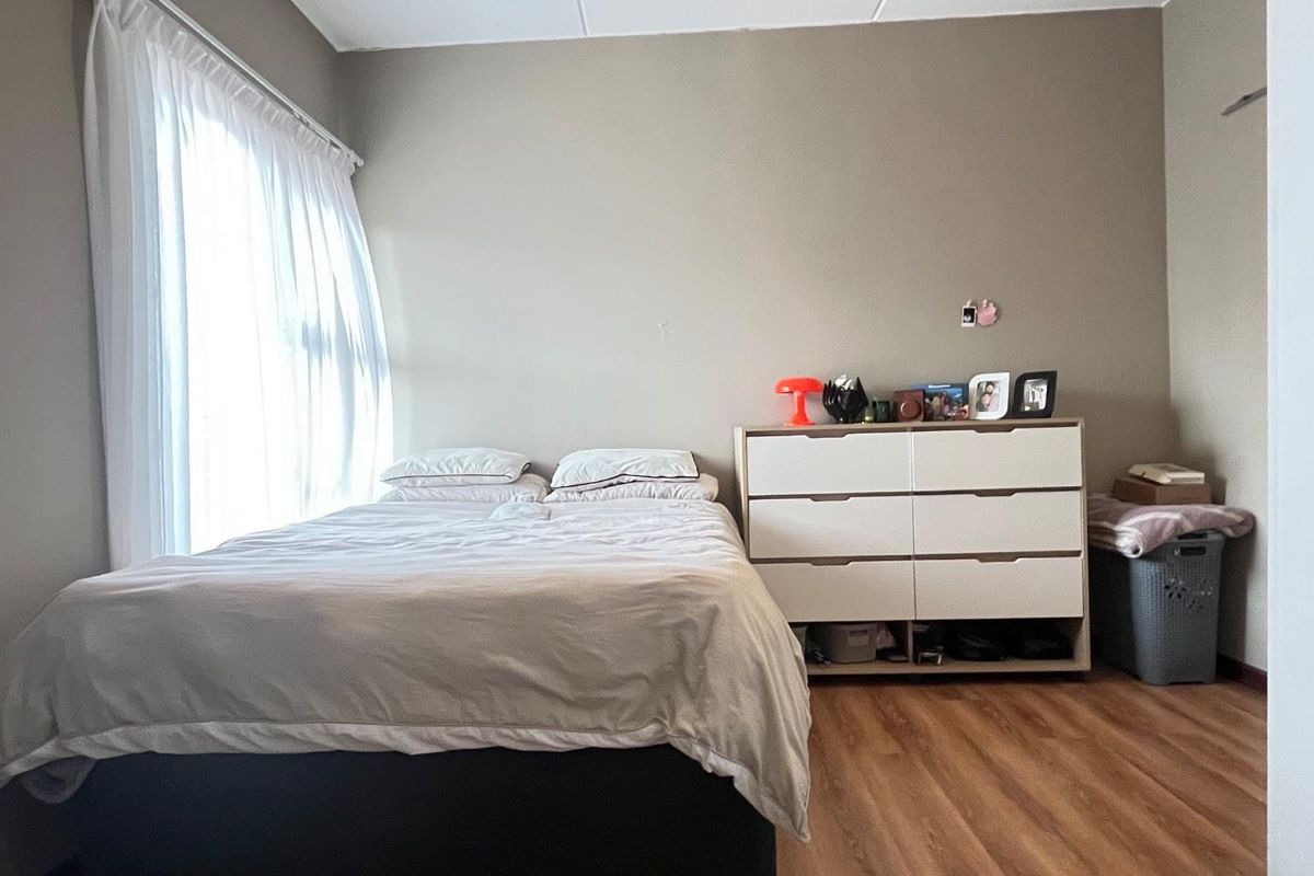 A functional bedroom featuring laminate flooring and a window with a curtain rail, offering a neutral base for personalization.