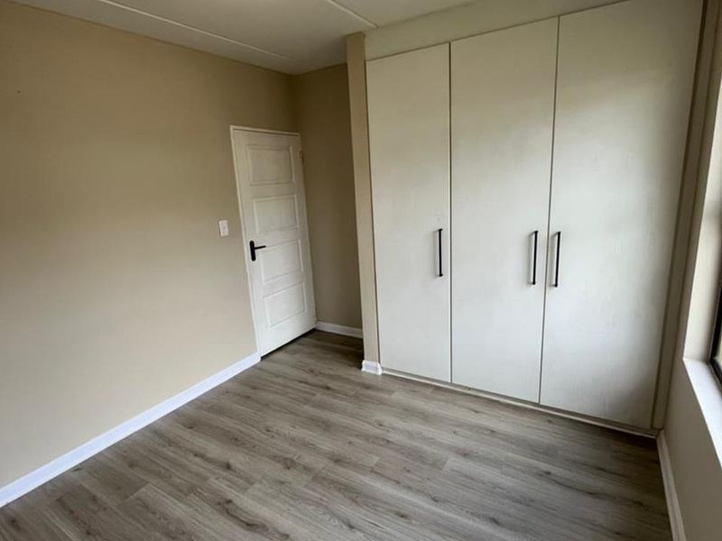 A clean, empty bedroom featuring modern laminate flooring and ample built-in cupboard storage space.