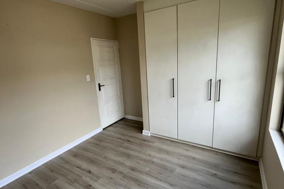A clean, empty bedroom featuring modern laminate flooring and ample built-in cupboard storage space.