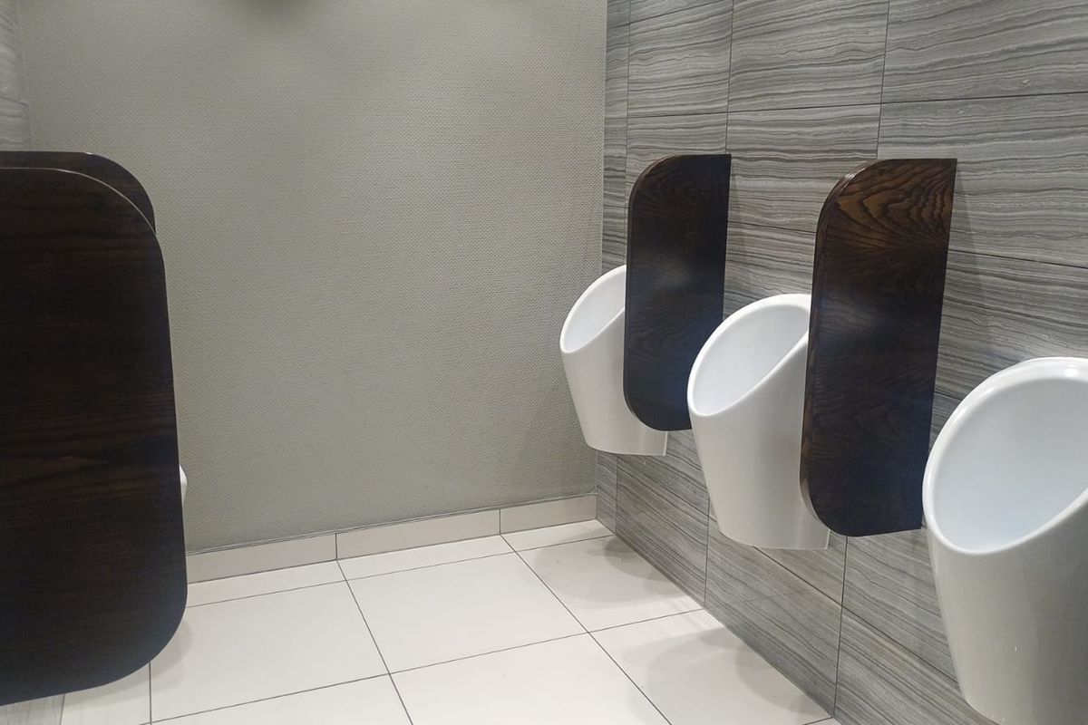 A clean, modern office restroom featuring wall-mounted urinals with dark wood privacy partitions and contemporary grey tiled wall finishes.