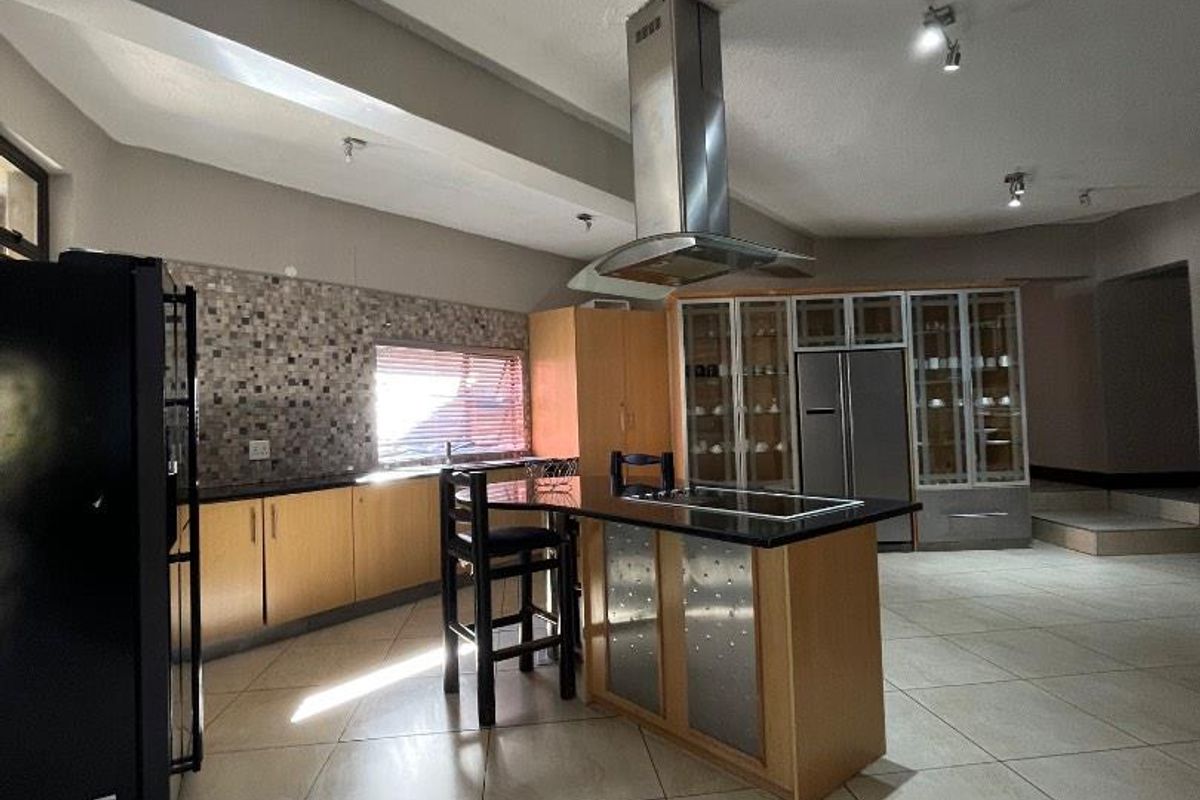 Spacious kitchen featuring a central island with a built-in hob, stainless steel extractor fan, stone countertops, and extensive cabinetry with a mosaic tile backsplash.