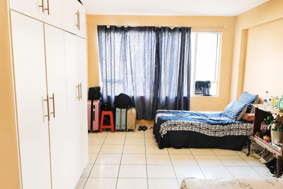 A bedroom featuring tiled flooring and a large white built-in wardrobe, offering functional storage space.