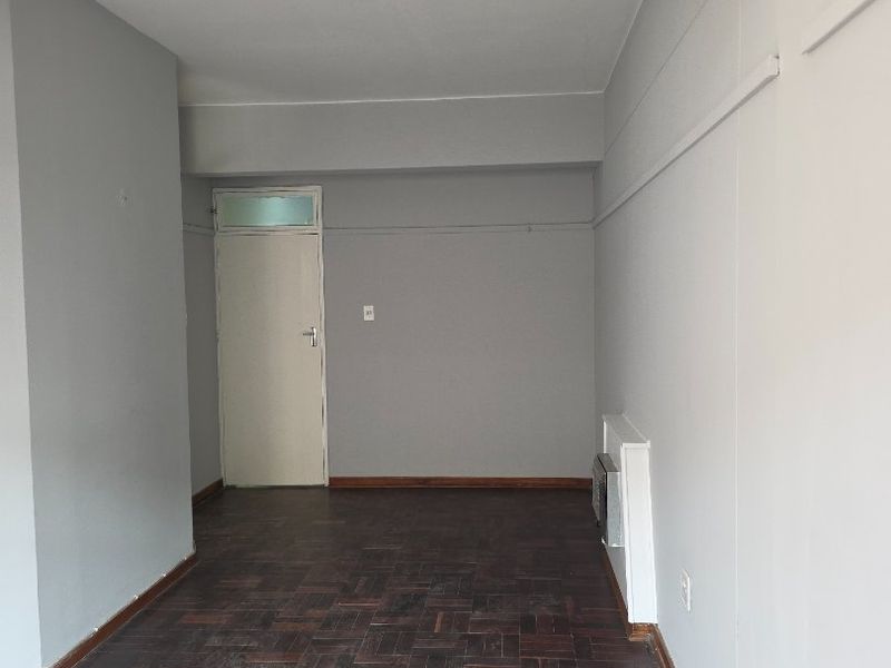 An empty living area featuring dark parquet flooring and neutral grey walls, providing a blank canvas for interior design.