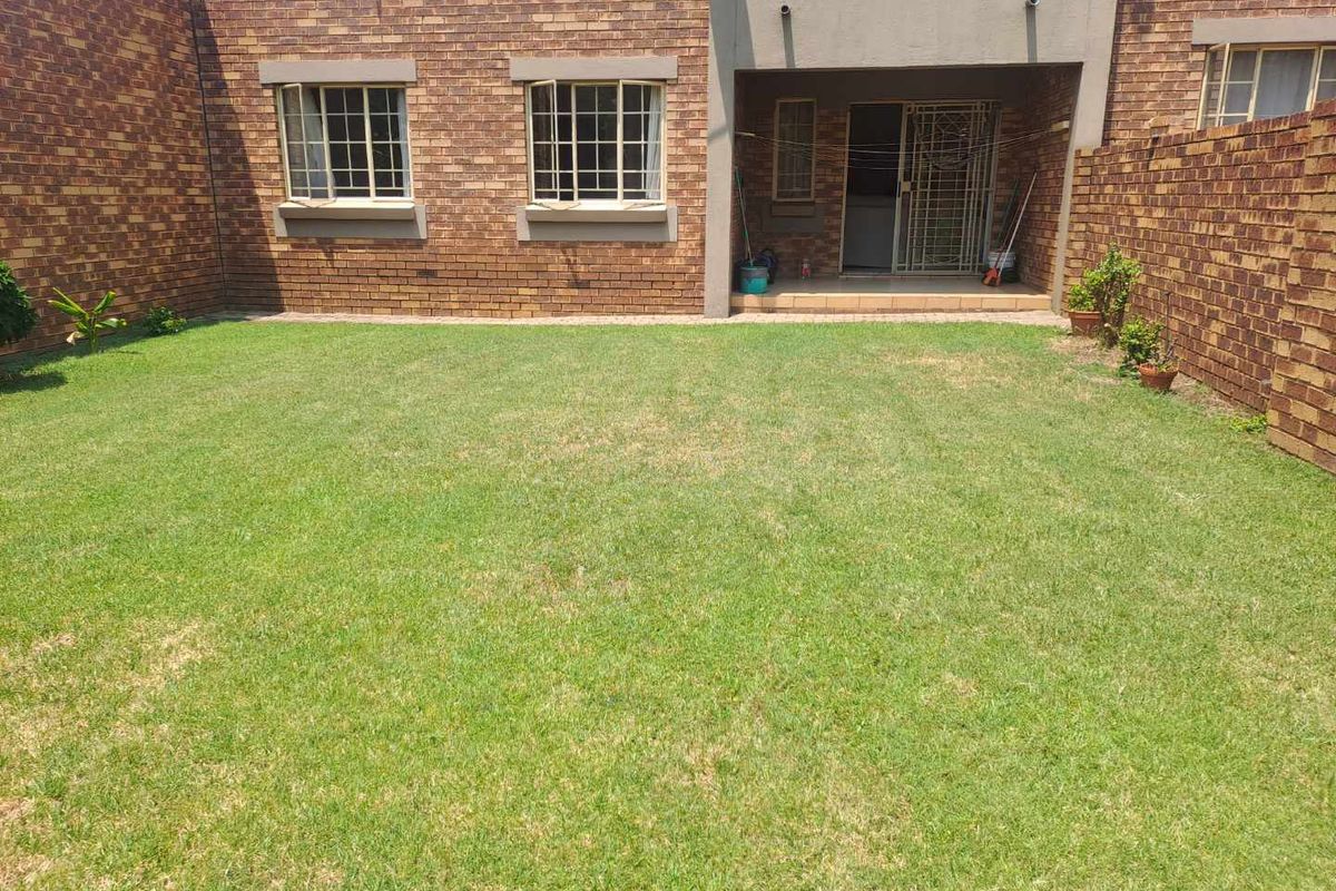 A private rear garden featuring a level lawn area, brick boundary walls, and direct access to the apartment via a covered patio.