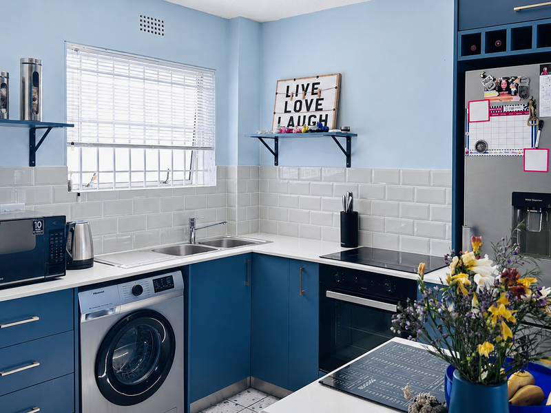 Modern kitchen featuring blue cabinetry, subway tile backsplash, integrated oven and hob, and stainless steel sink with ample counter space.