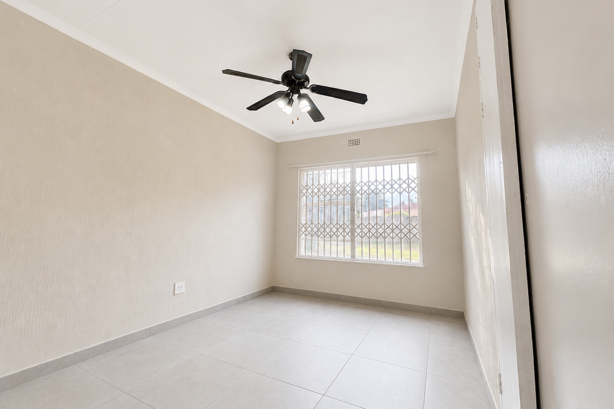 A bright, empty bedroom featuring neutral tiled flooring, a ceiling fan, and a security gate on the window.
