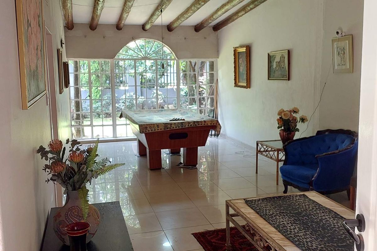 Spacious living area featuring exposed timber ceiling beams, large arched window, and polished floor tiles, offering a bright and versatile entertainment space.