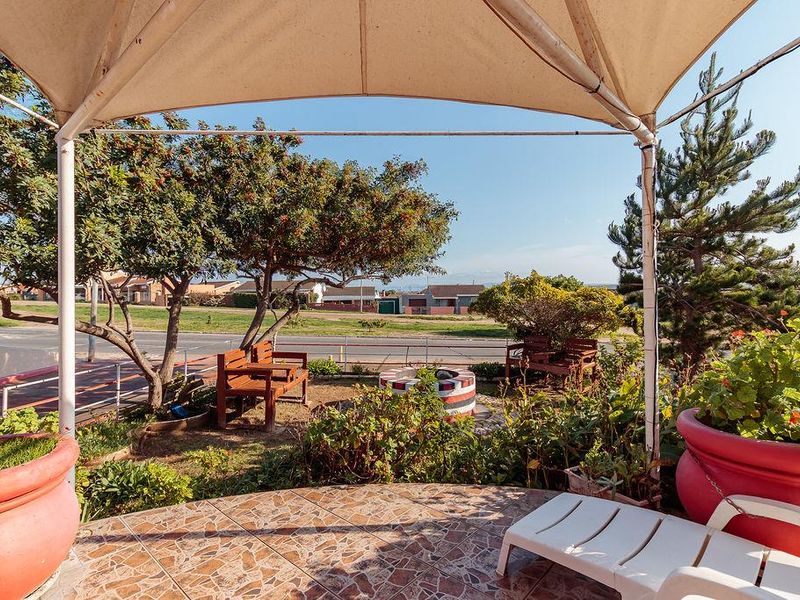 A covered outdoor patio area featuring tiled flooring, a built-in fire pit, and a shade canopy, overlooking a residential street.