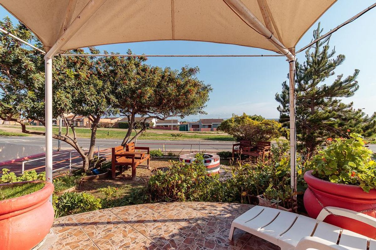 A covered outdoor patio area featuring tiled flooring, a built-in fire pit, and a shade canopy, overlooking a residential street.