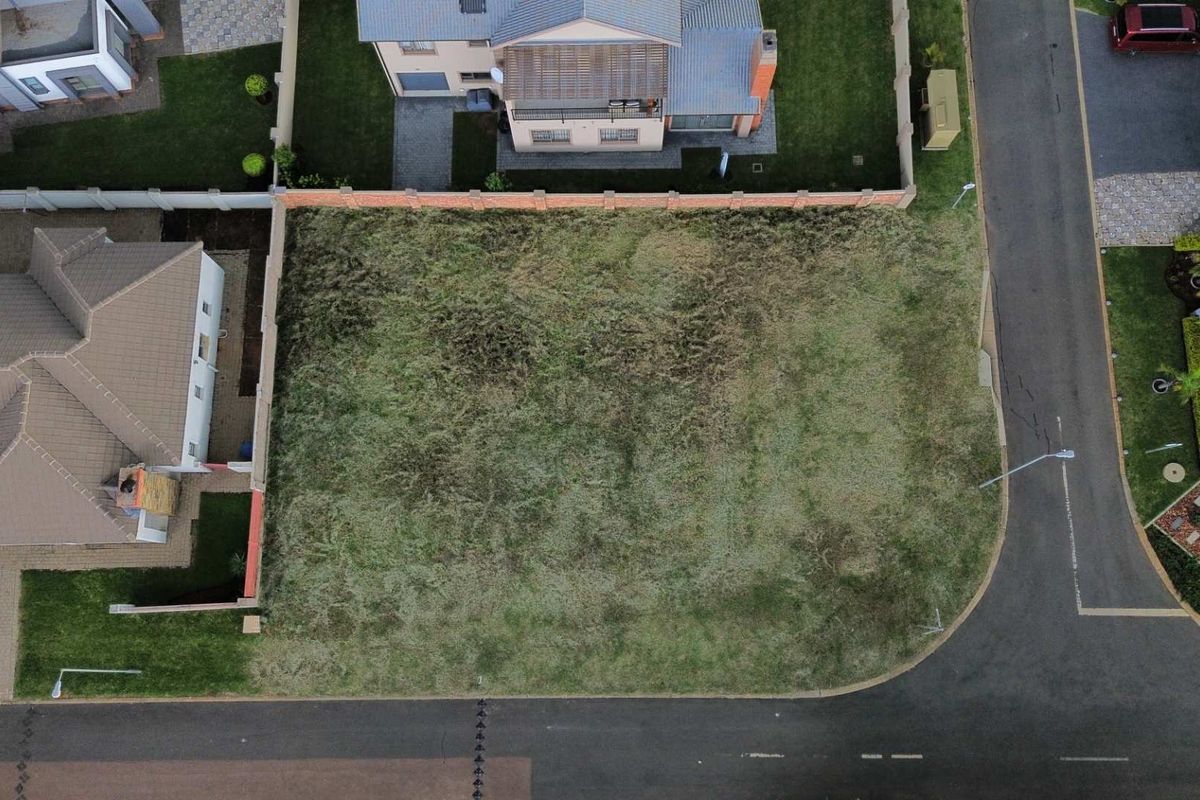 Aerial view of a vacant residential plot situated in a developed neighborhood, featuring established boundary walls and street access.