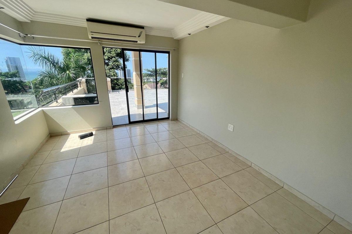 An empty living area featuring tiled flooring, crown molding, a wall-mounted air conditioning unit, and sliding glass doors leading to a balcony.