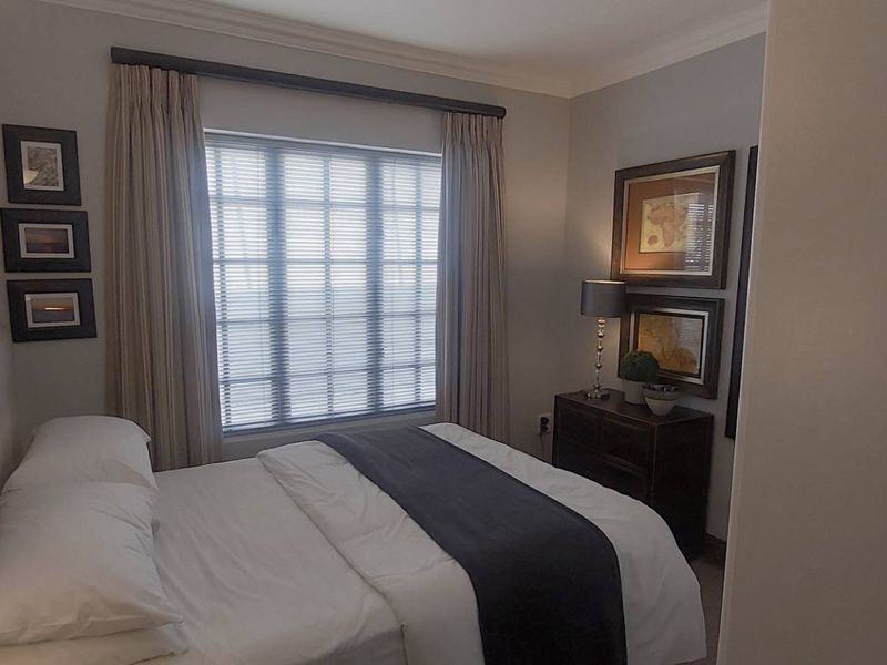 A well-maintained bedroom featuring neutral wall tones, crown molding, and a large window with fitted curtains.