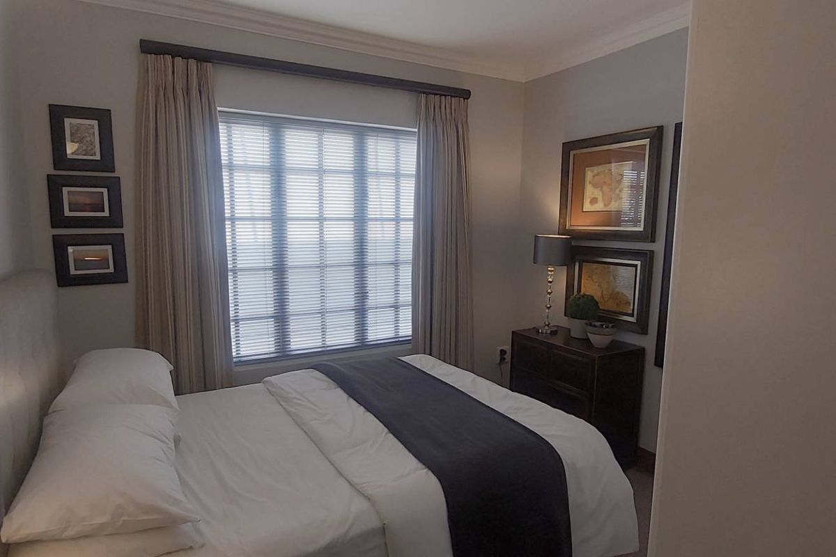 A well-maintained bedroom featuring neutral wall tones, crown molding, and a large window with fitted curtains.