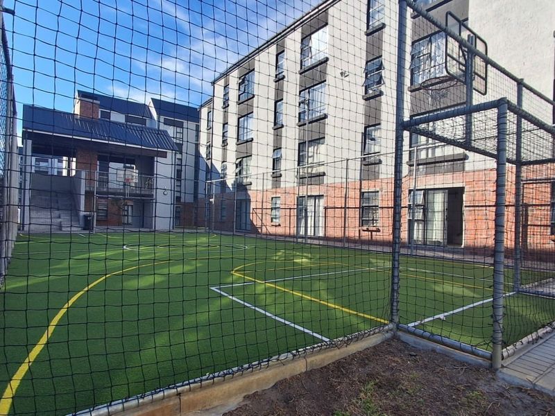 A well-maintained outdoor sports facility featuring artificial turf, goal posts, and secure perimeter fencing within the apartment complex grounds.