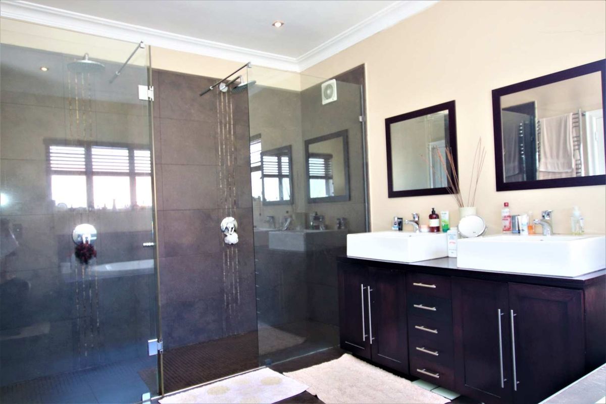 Modern bathroom featuring a spacious walk-in glass shower with dark tiling and a double vanity with vessel sinks and dark cabinetry.