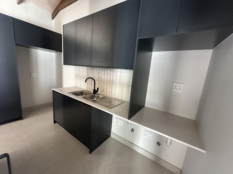 Modern scullery featuring sleek black cabinetry, stone countertops, a stainless steel double sink with a black mixer tap, and dedicated appliance plumbing connections.