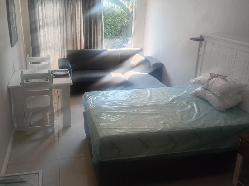 An open-plan studio apartment featuring tiled flooring and a sliding glass door providing natural light.