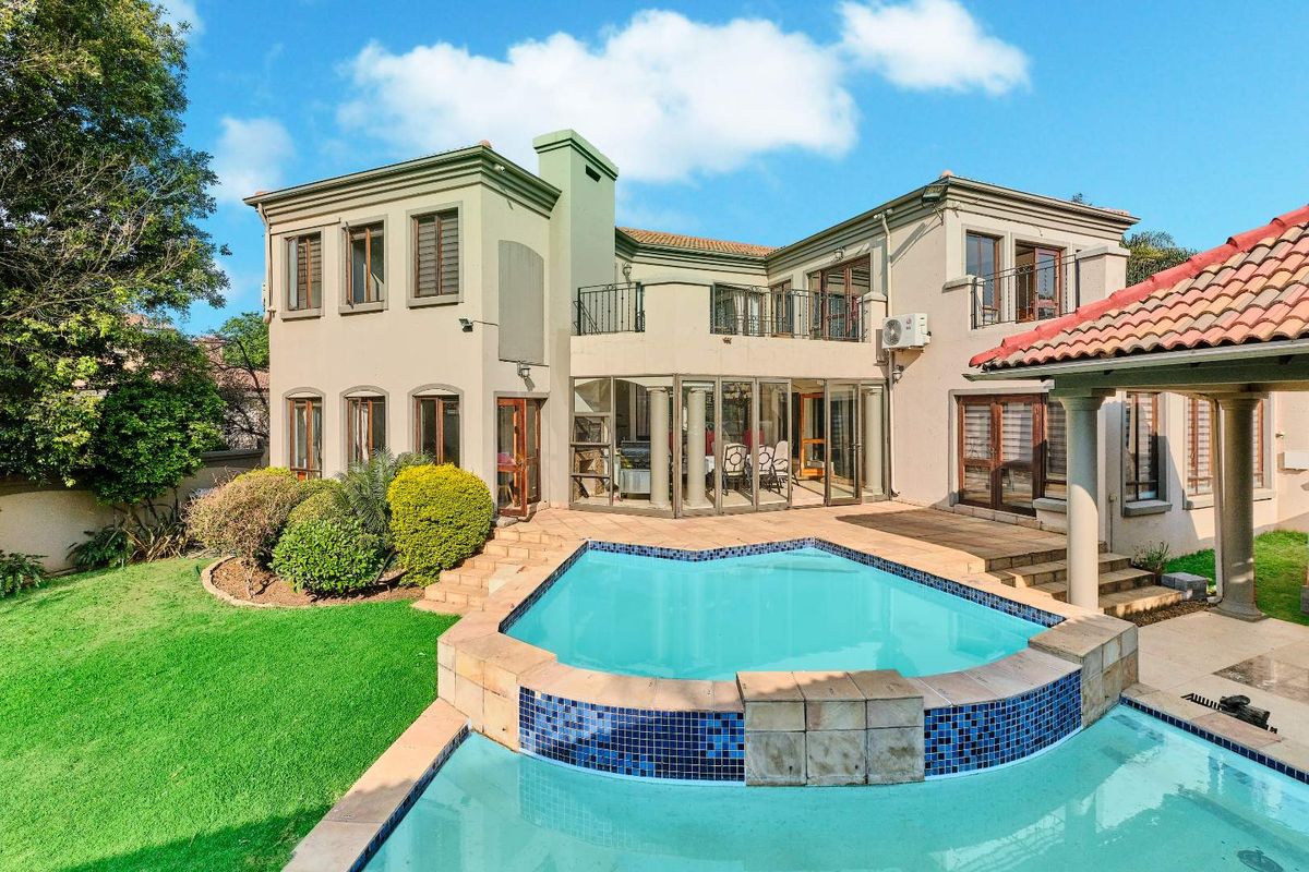 Rear view of the property featuring a swimming pool, paved patio area, and a two-story building with balconies and large glass doors.