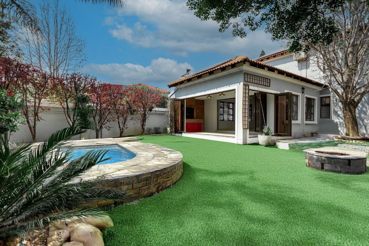 A well-maintained rear garden featuring a swimming pool, artificial lawn, and a covered patio area with built-in braai facilities.