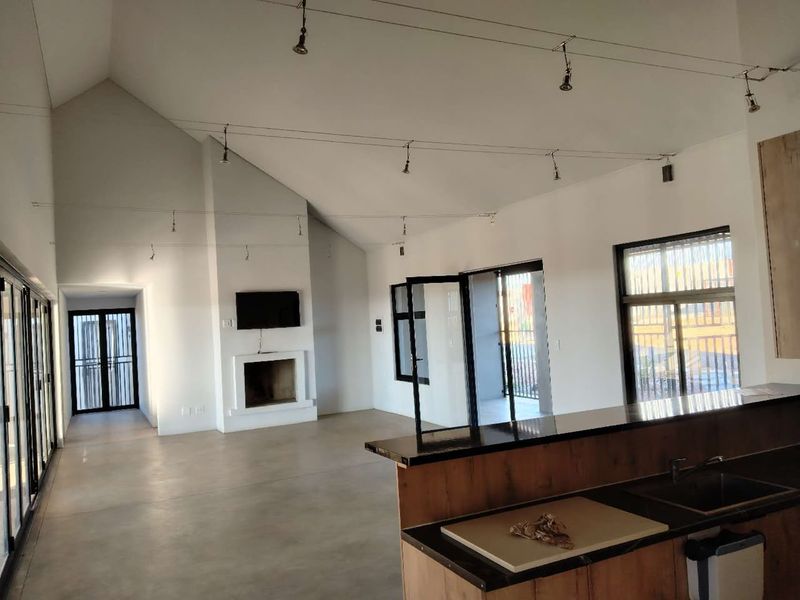 Spacious open-plan living area featuring a vaulted ceiling, polished concrete floors, a built-in fireplace, and a modern kitchen island with integrated sink.