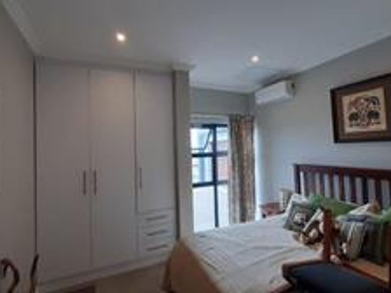 A well-maintained bedroom featuring built-in cupboards, recessed downlighting, and a wall-mounted split-system air conditioner, providing a comfortable and functional living space.