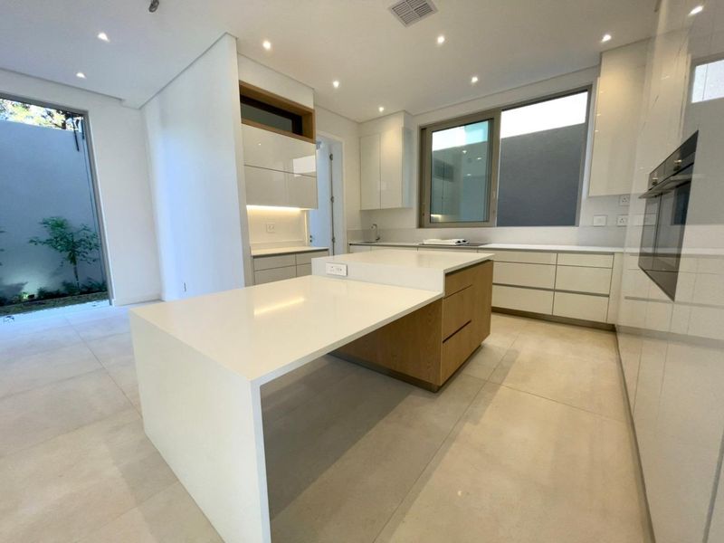 Modern kitchen featuring sleek white cabinetry, a central island with a breakfast bar, integrated oven, and large format floor tiles.