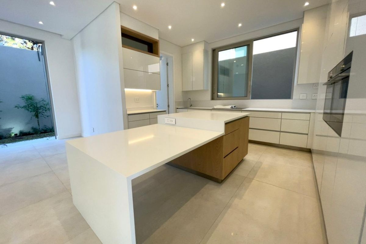 Modern kitchen featuring sleek white cabinetry, a central island with a breakfast bar, integrated oven, and large format floor tiles.