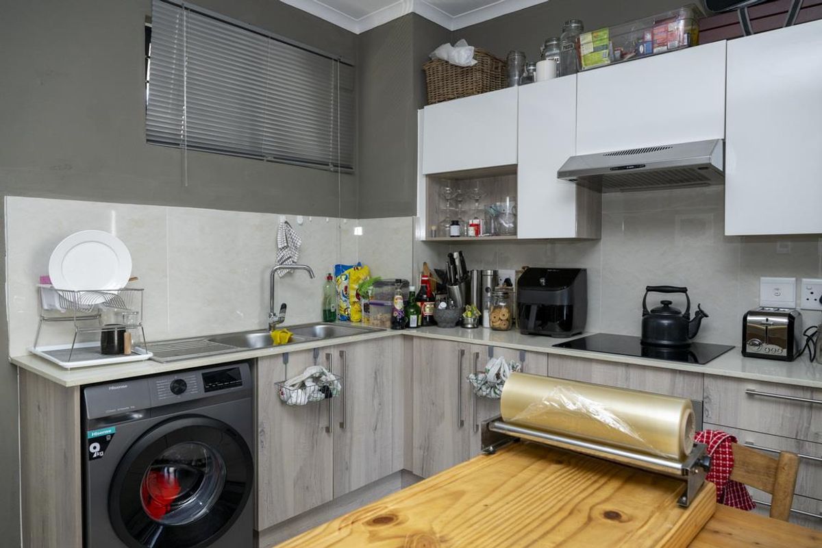 Compact kitchen featuring light wood-grain cabinetry, integrated washing machine, stainless steel sink, and built-in electric hob with extractor fan.