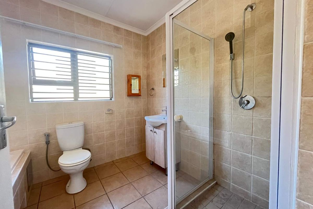 A functional bathroom featuring a shower enclosure, toilet, and vanity basin with neutral wall and floor tiling.