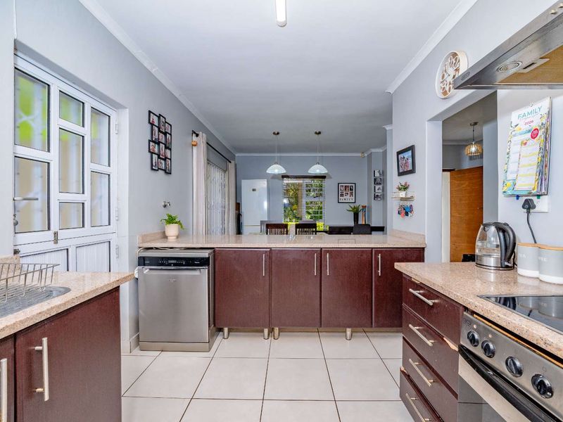 Open-plan kitchen and dining area featuring dark wood cabinetry, granite countertops, stainless steel appliances, and neutral tiled flooring.