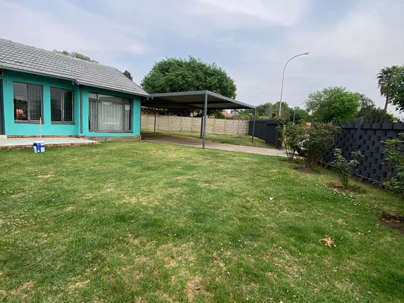 A spacious rear garden featuring a large lawn, a paved driveway, and a covered carport structure.