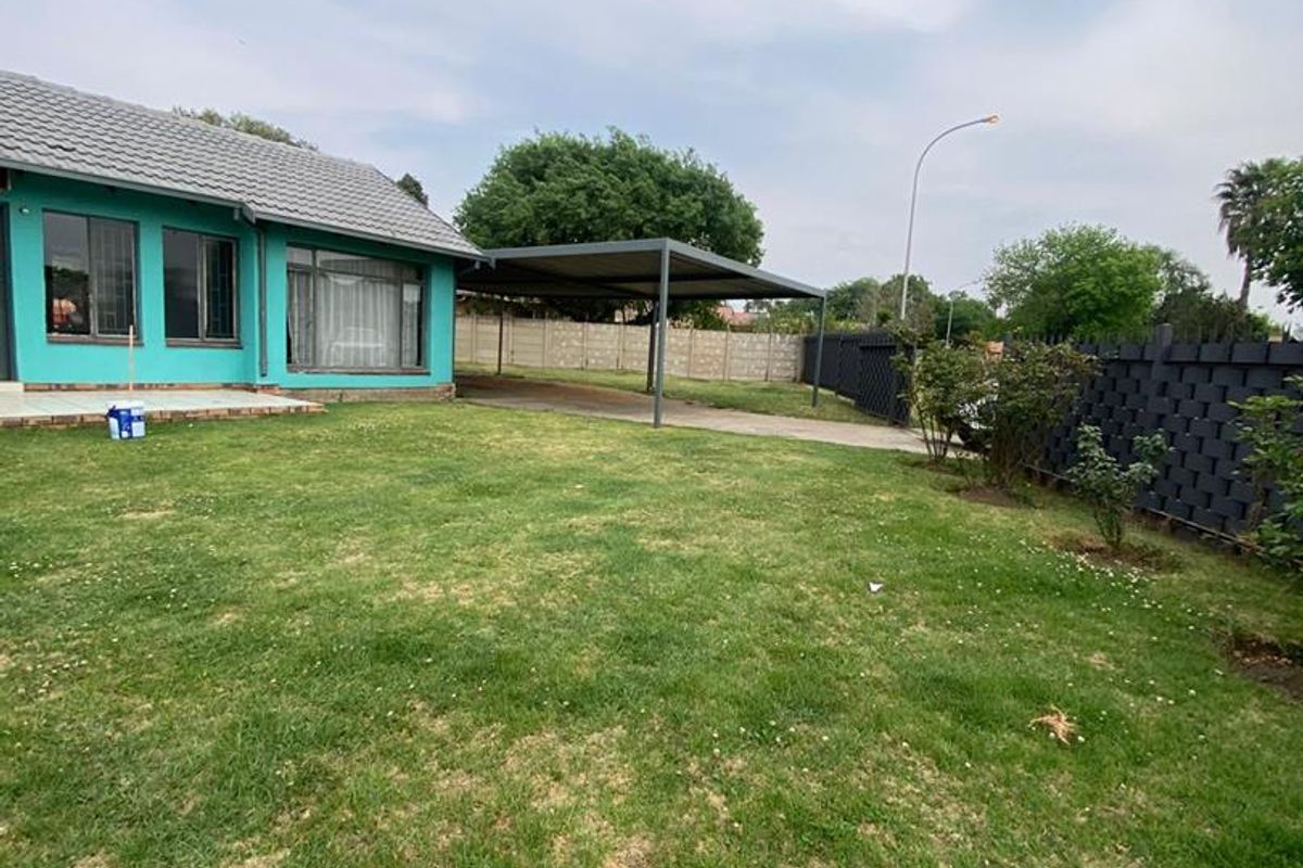 A spacious rear garden featuring a large lawn, a paved driveway, and a covered carport structure.