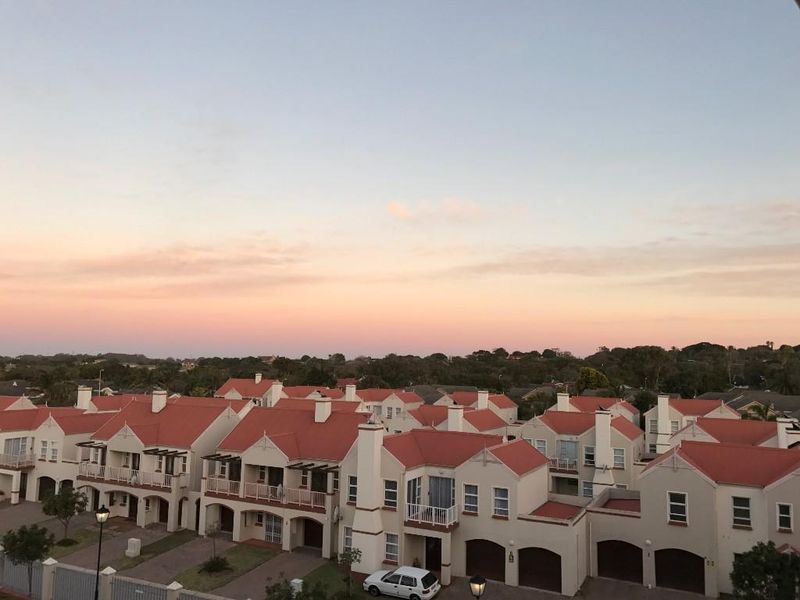 An elevated view overlooking a residential complex featuring uniform architecture with pitched terracotta roofs and balconies at sunset.