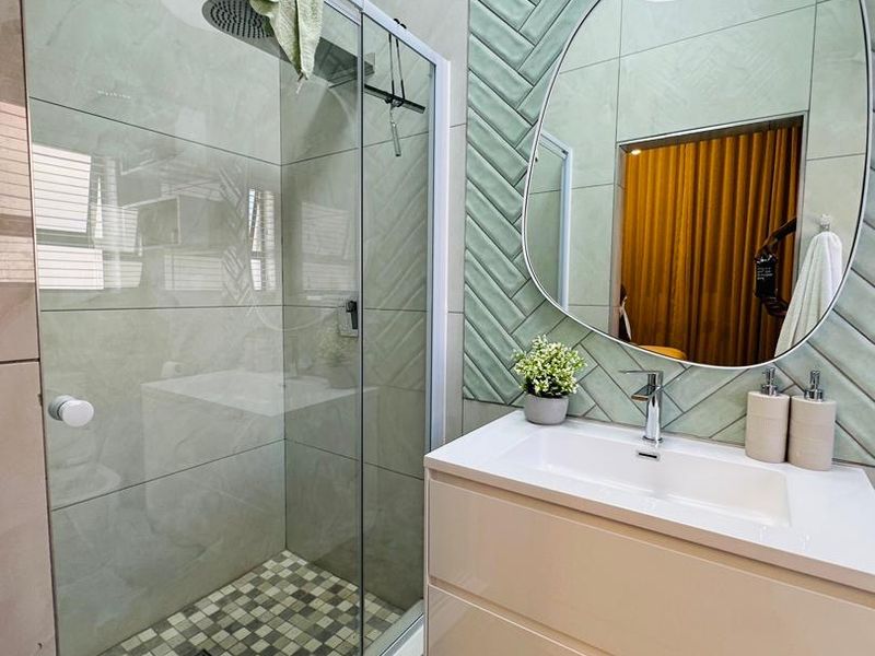 Modern bathroom featuring a glass-enclosed shower with a rain shower head and a contemporary wall-mounted vanity with stylish herringbone feature tiling.