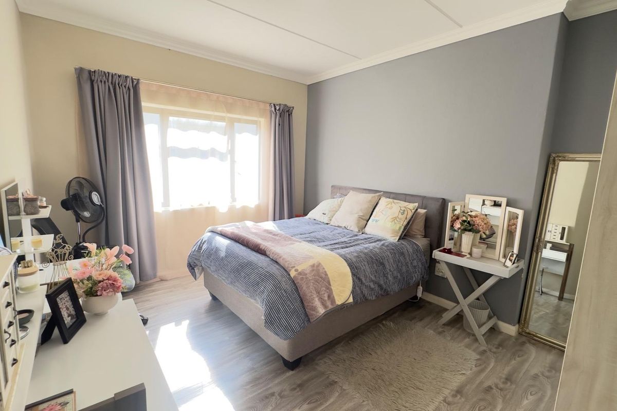 A well-maintained bedroom featuring light wood-look laminate flooring, a neutral color palette, and a large window allowing for ample natural light.