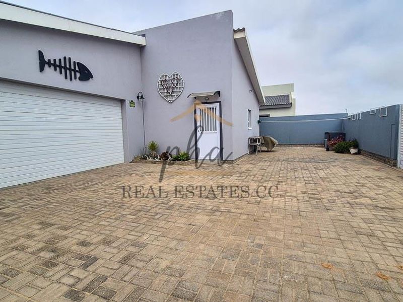 A paved driveway leading to a garage and entrance, featuring a secure boundary wall and exterior facade.