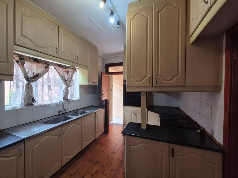 A functional kitchen featuring dated built-in cabinetry, laminate countertops, a double stainless steel sink, and a built-in hob with direct access to the exterior.
