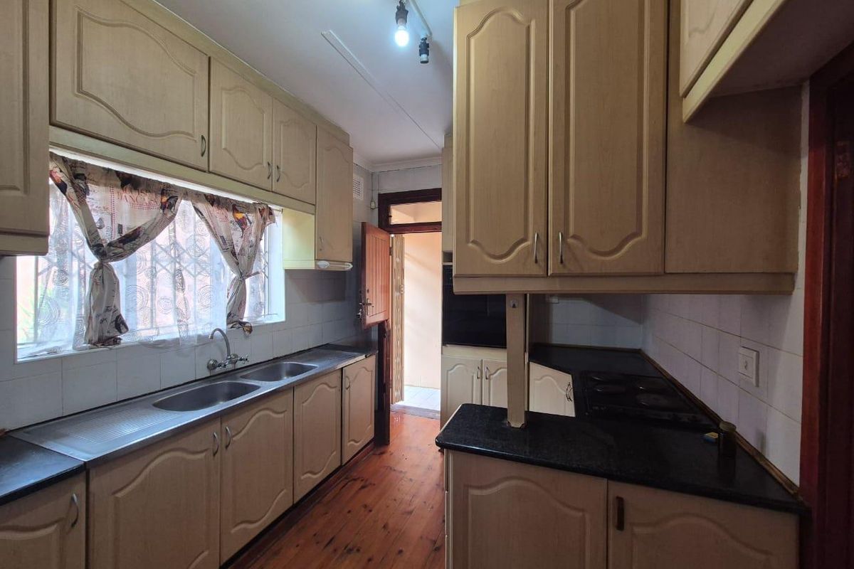 A functional kitchen featuring dated built-in cabinetry, laminate countertops, a double stainless steel sink, and a built-in hob with direct access to the exterior.