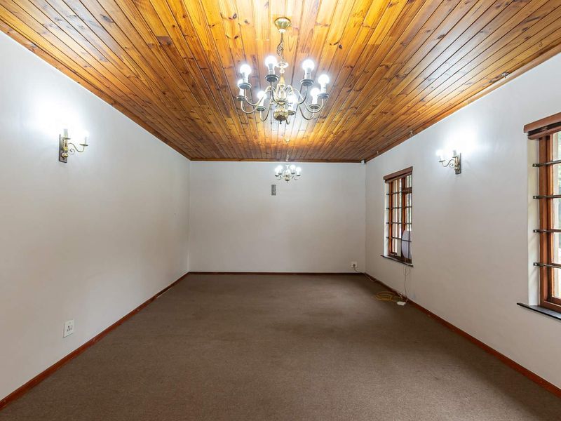 Spacious living area featuring a timber tongue and groove ceiling, classic chandelier lighting, and large windows with security bars.