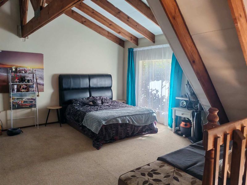 Spacious bedroom featuring a pitched ceiling with exposed timber rafters and a sliding glass door providing natural light.