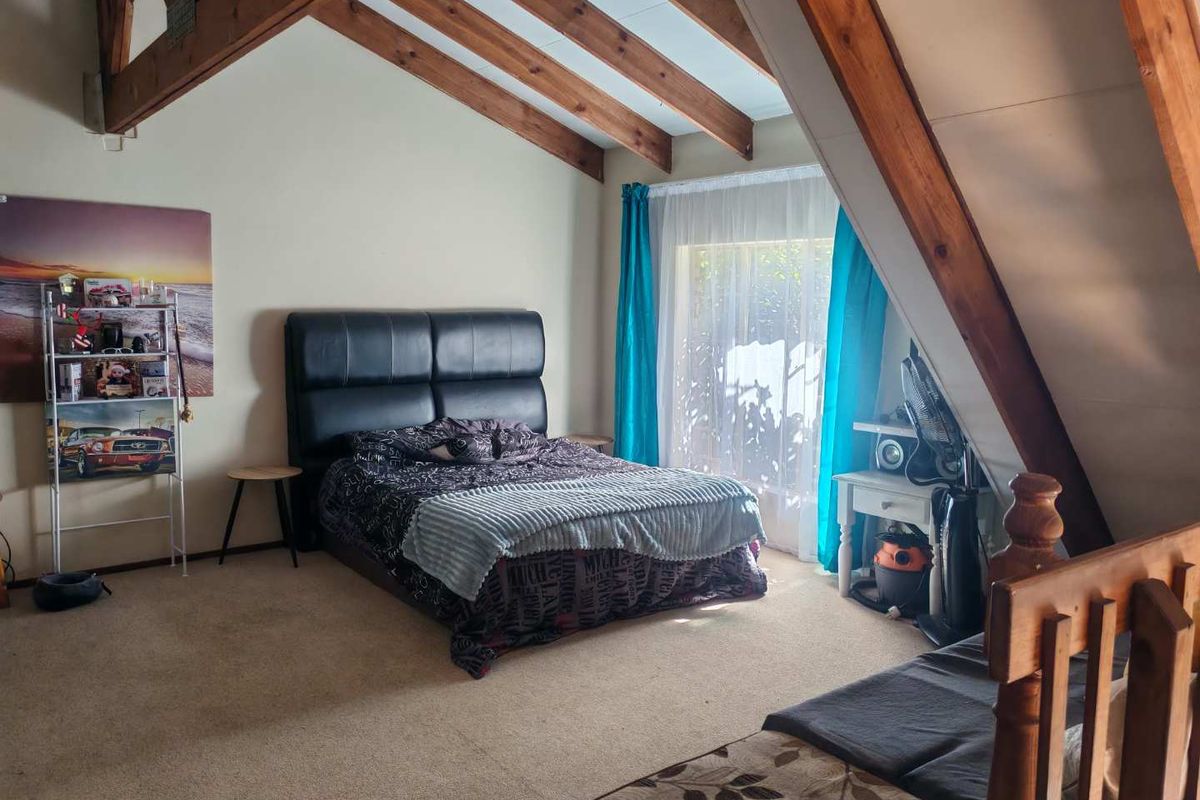 Spacious bedroom featuring a pitched ceiling with exposed timber rafters and a sliding glass door providing natural light.