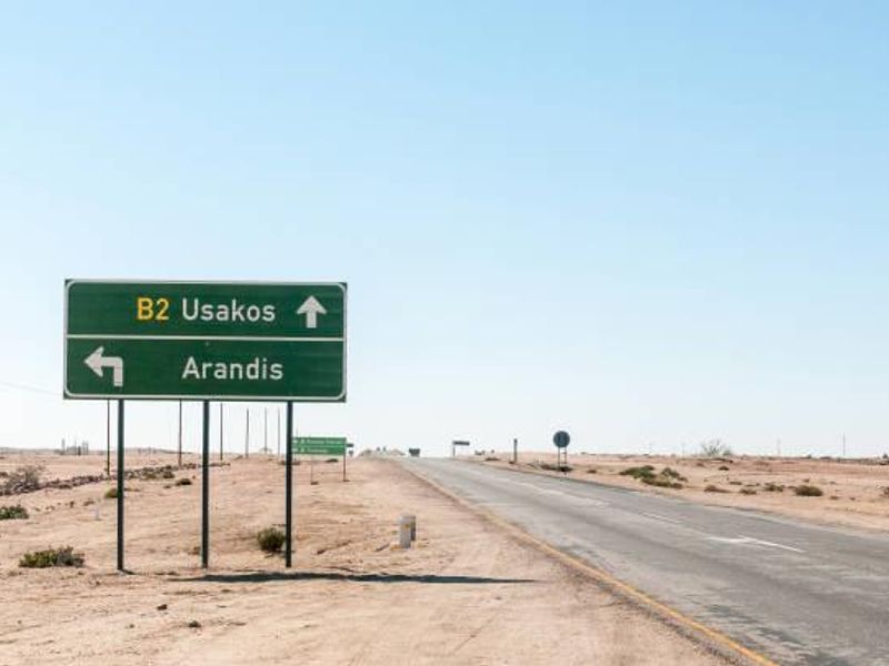 A view of a desert road with directional signage indicating routes to Usakos and Arandis.