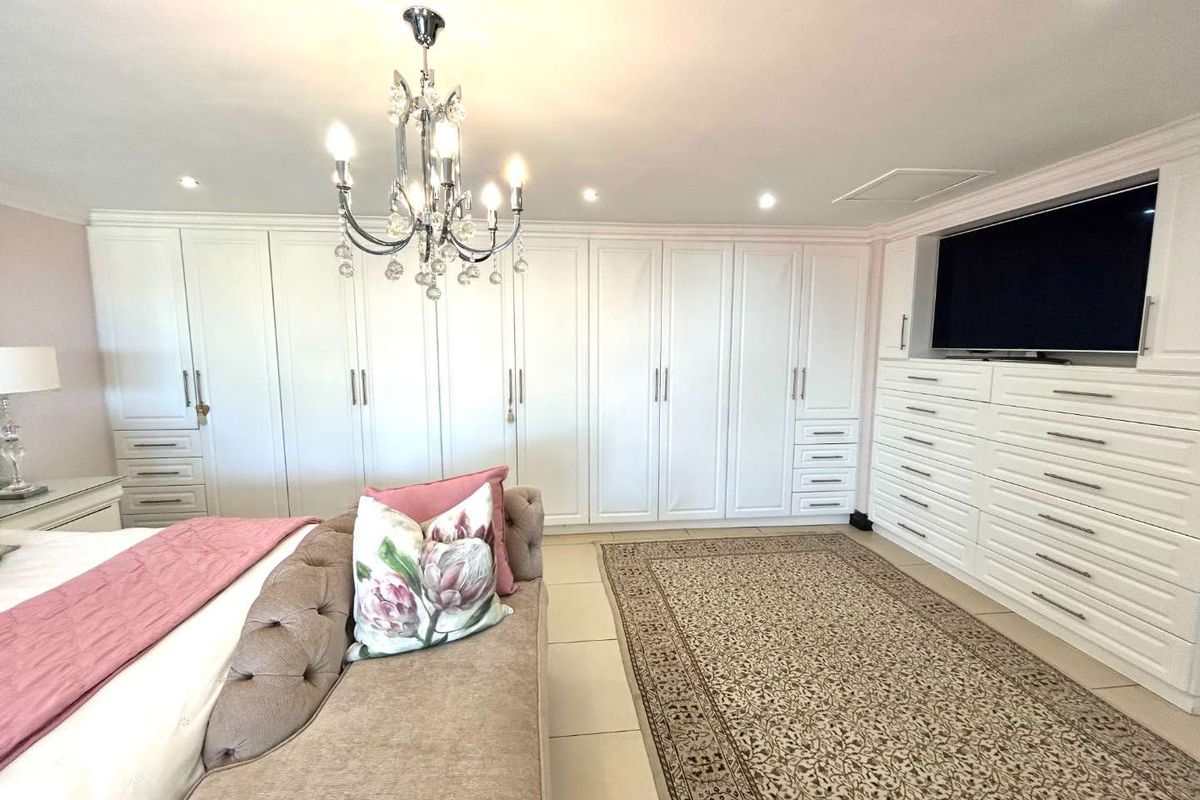 Spacious bedroom featuring extensive white built-in wardrobes, integrated cabinetry, tiled flooring, and a decorative chandelier.