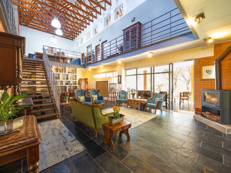 Spacious double-volume living area featuring exposed timber trusses, a mezzanine level, slate flooring, and a modern freestanding fireplace with access to the patio.