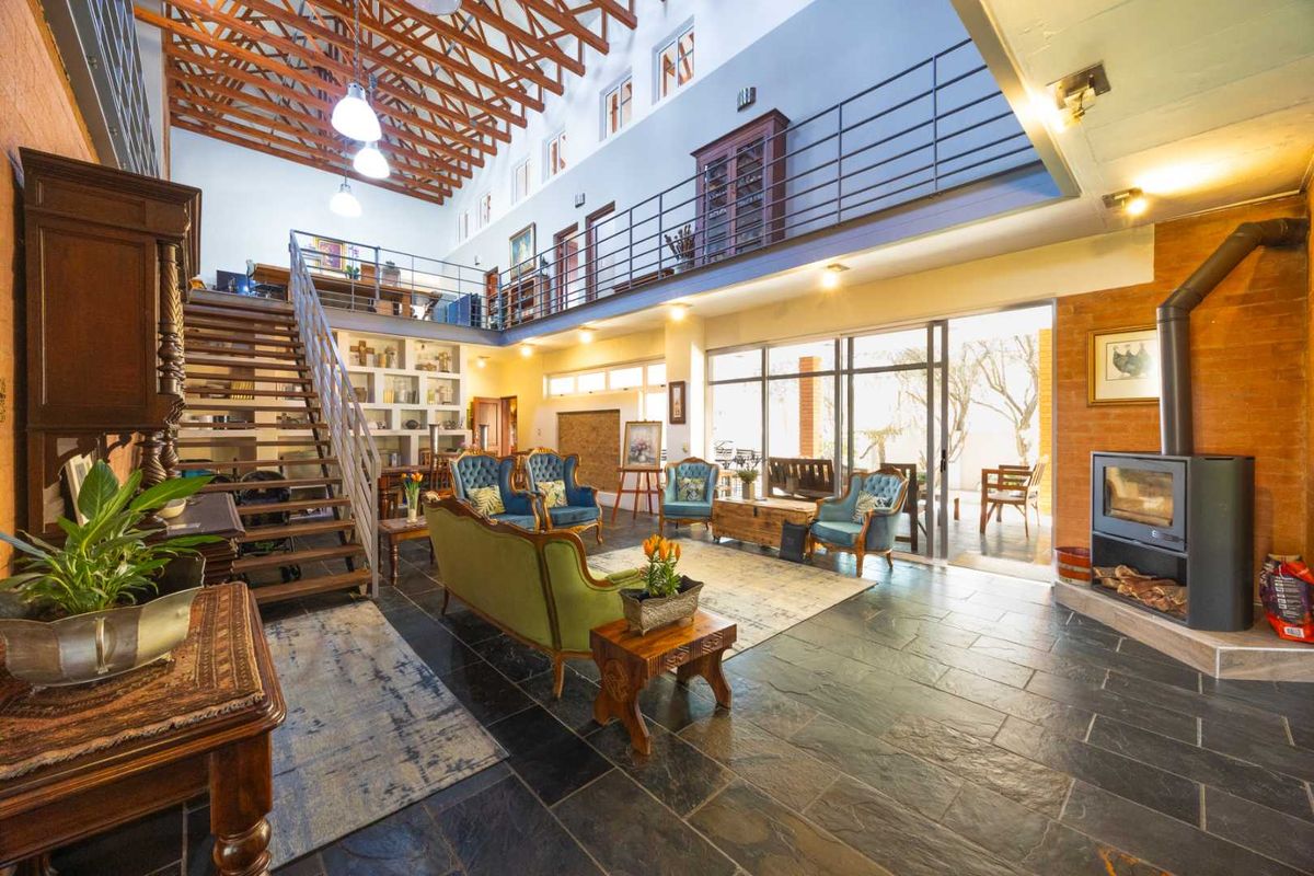 Spacious double-volume living area featuring exposed timber trusses, a mezzanine level, slate flooring, and a modern freestanding fireplace with access to the patio.