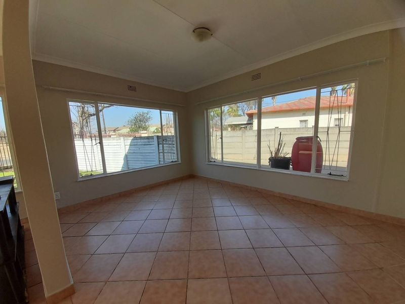 A bright, empty living room featuring neutral wall tones, large windows with security bars, and tiled flooring throughout.