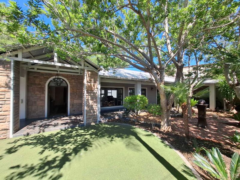 Front entrance area featuring stone cladding, a covered porch with tiled flooring, and an arched doorway, set within a landscaped garden with artificial lawn.